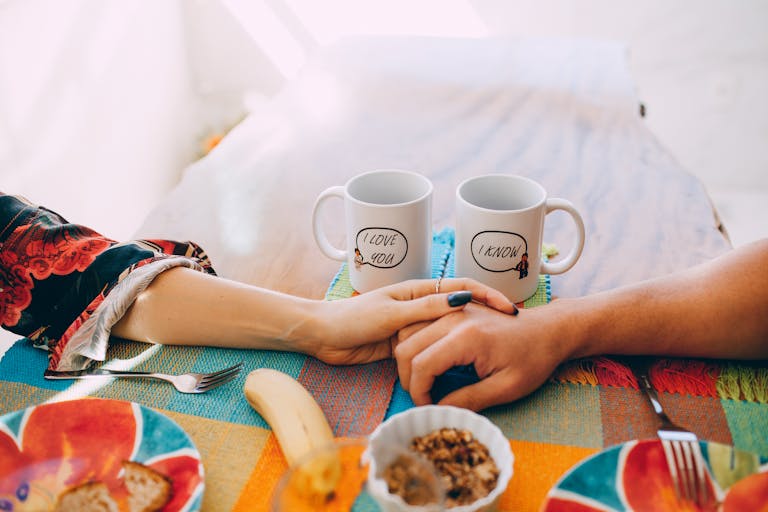Crackstube A cozy breakfast scene with two mugs, holding hands, and a colorful table setting.