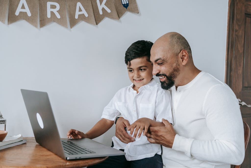 join-myquiz.org A father and son smiling while using a laptop, creating a moment of joy and bonding indoors.