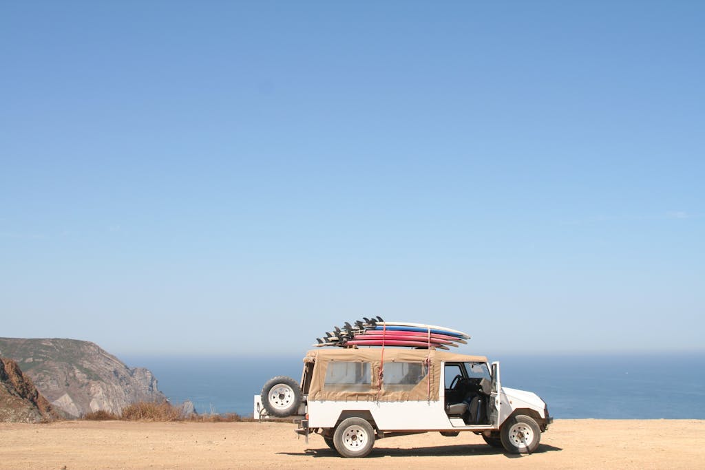 hj54kyf:  A jeep loaded with surfboards parked by a scenic ocean cliff under a clear sky.