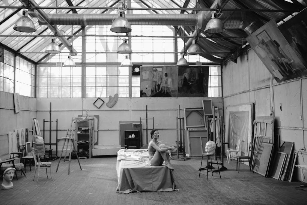 Messeregge A nude woman posing in a sunlit art studio surrounded by easels and paintings.