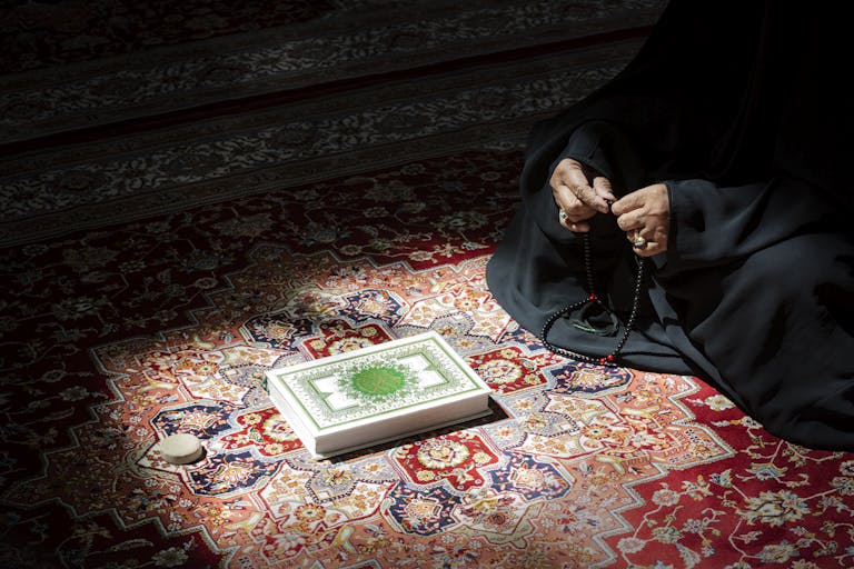Trios 5 Invisalign Submission A woman in serene prayer holding beads beside an ornate Quran on a colorful rug.