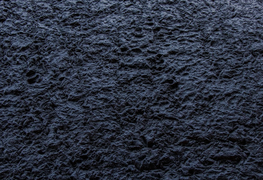Chatpic Close-up of a dark, rough textured stone surface providing an abstract background.