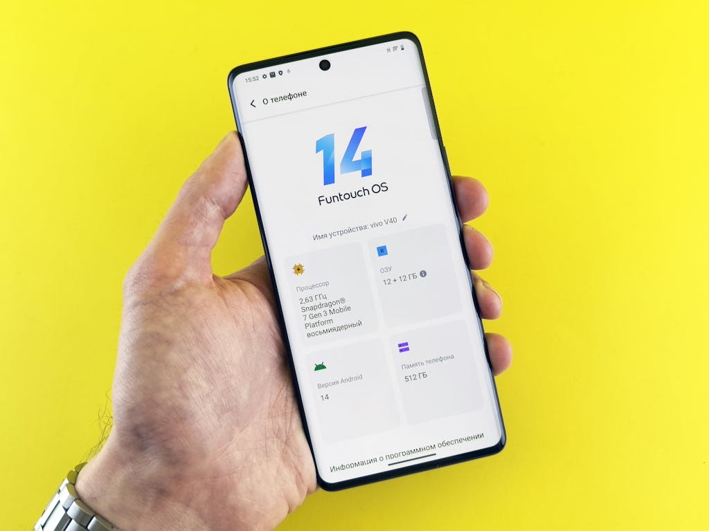 Kongotech Org Close-up of a hand holding a smartphone displaying Funtouch OS 14 on a vibrant yellow background.
