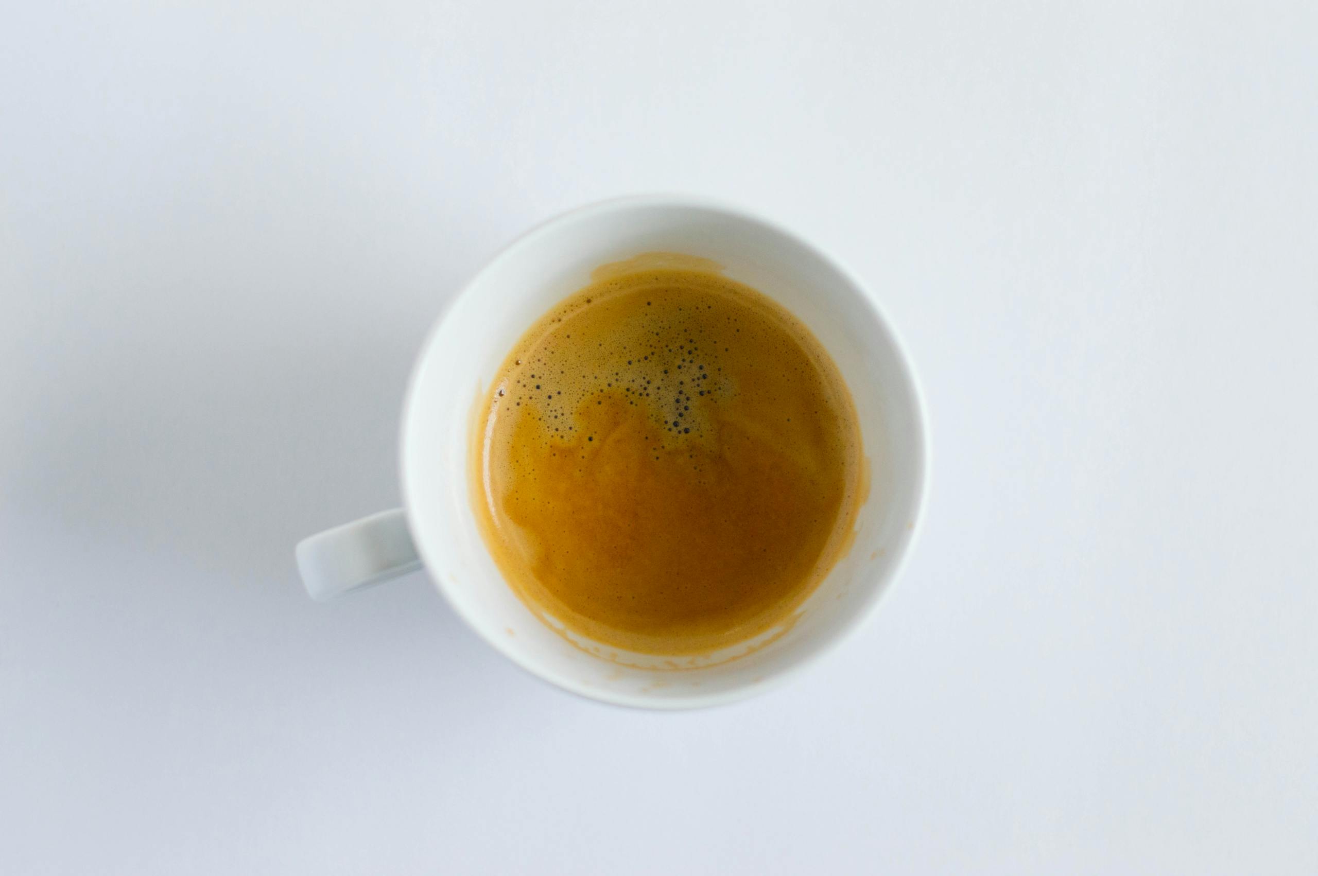 Bolly4u Me Minimalist top-down photo of a steaming cup of espresso in a white mug against a white background.