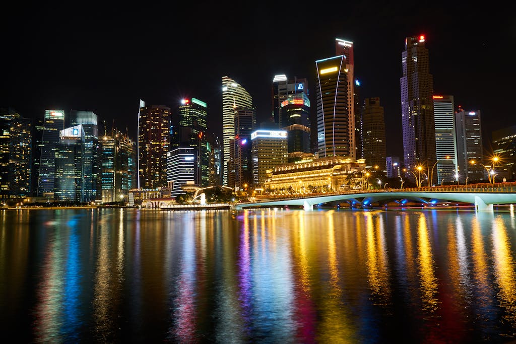 FintechAsia Night view of Singapore skyline reflected over Marina Bay with illuminated skyscrapers and vibrant lights.