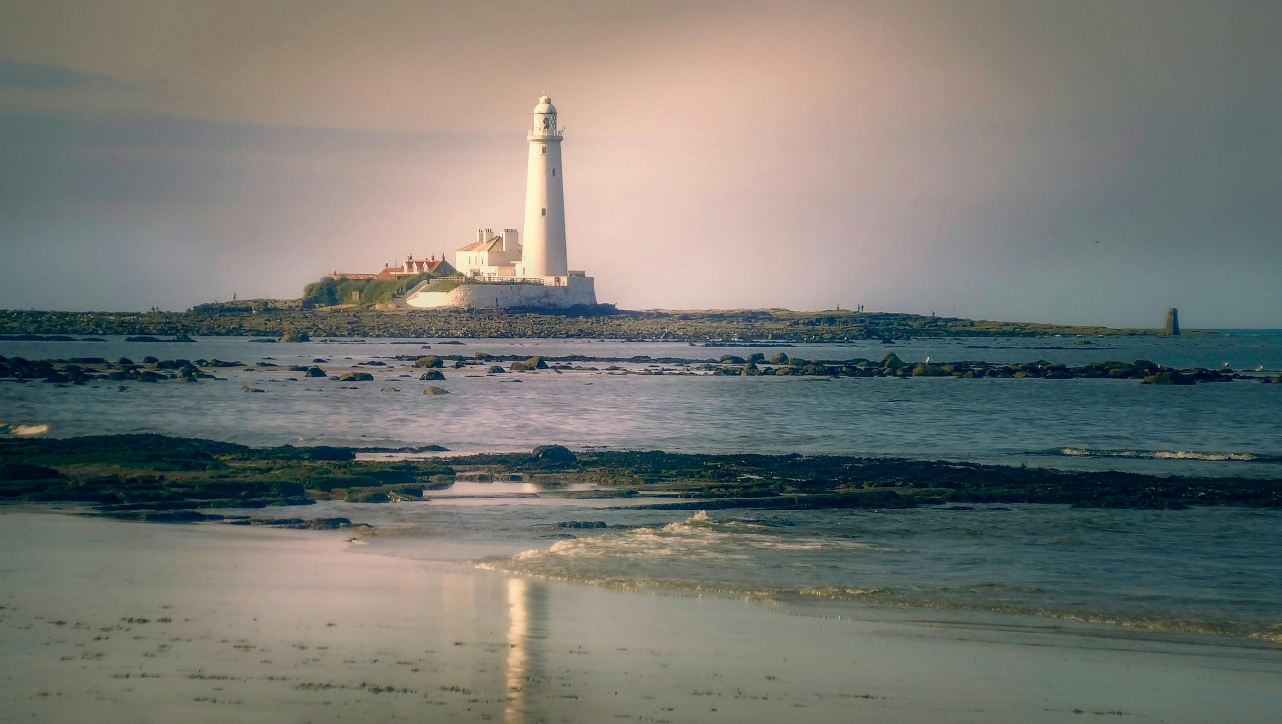 Mansutfer Peaceful scene of a lighthouse on a rocky beach at dawn, reflecting tranquility.
