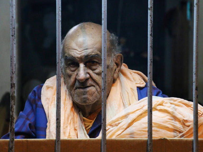 Hormita Portrait of an elderly man behind bars wearing casual clothing, conveying a thoughtful mood.
