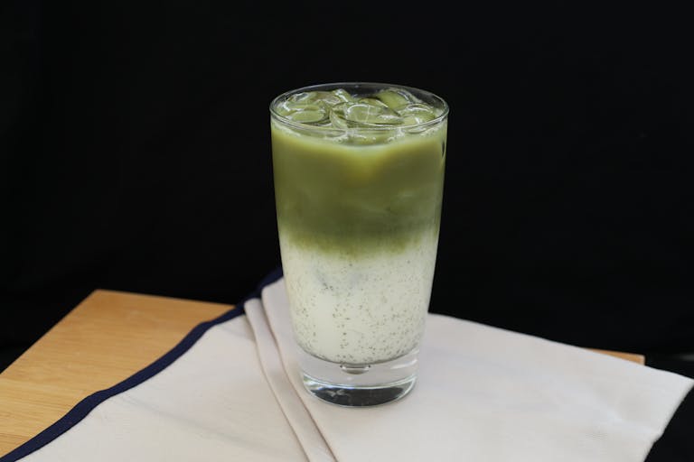 Bin Matcha Bin Matcha Refreshing iced matcha latte in a glass with milk on a wooden table.