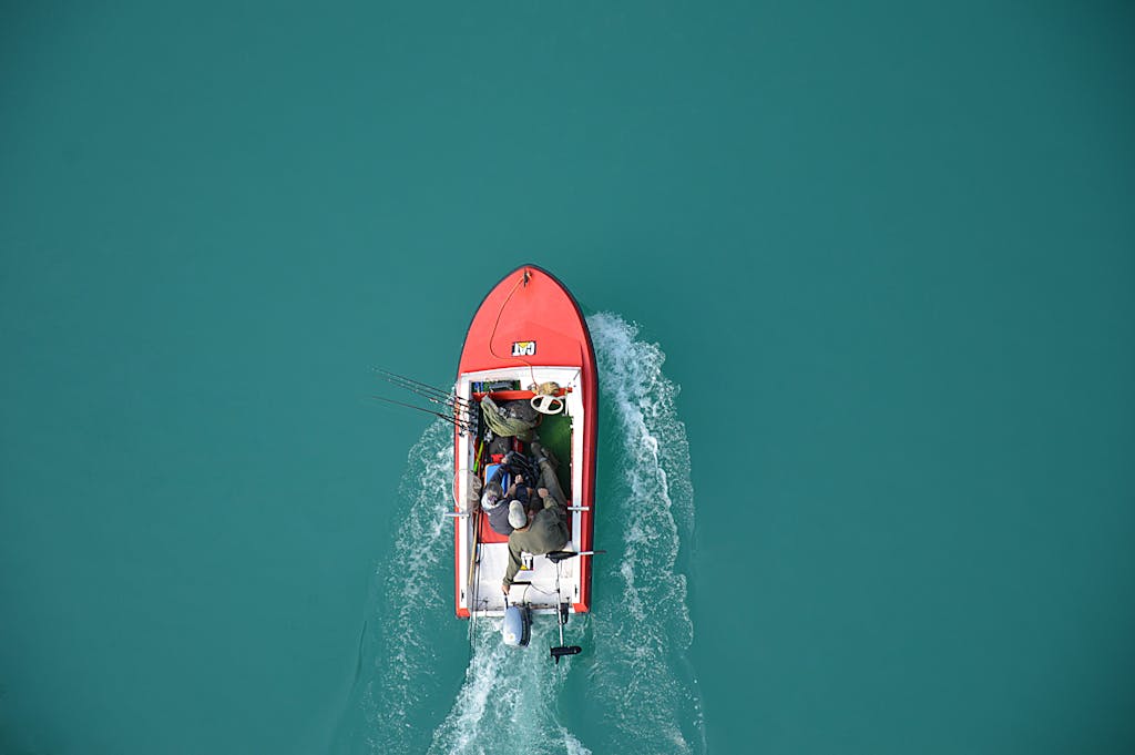 hj54kyf Top view of a red motorboat with fishermen navigating open turquoise waters.