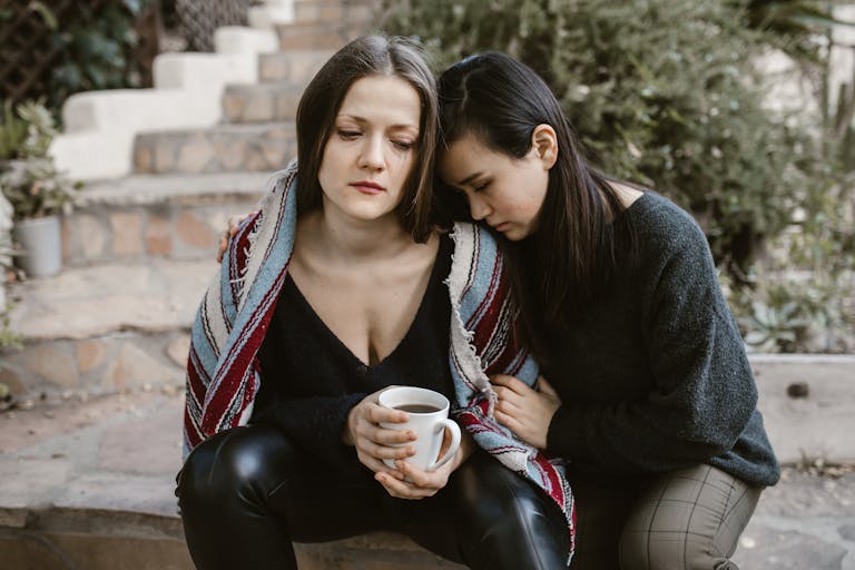 Understanding Wynonna Judd’s Performance Reactions Two women sitting closely, providing emotional support while holding a coffee cup.
