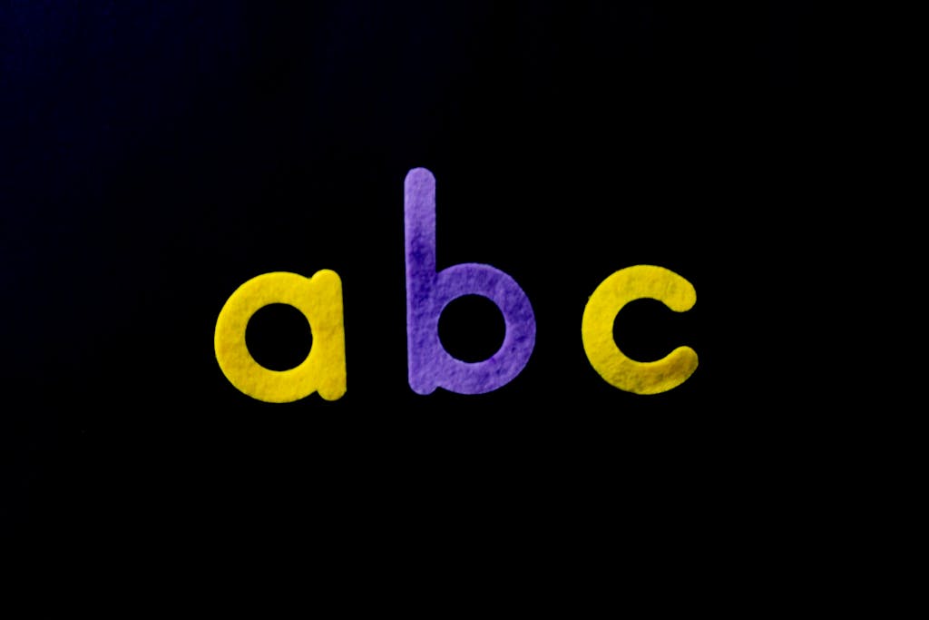 FamousParentingMomLife Vivid purple and yellow alphabet letters 'abc' on a black background, perfect for educational themes.