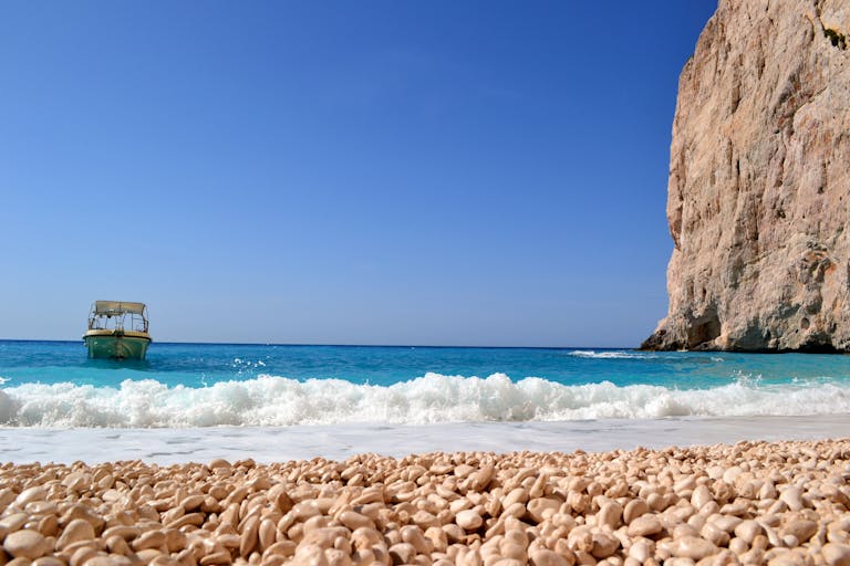 Voozon A peaceful seashore scene with a boat near a cliff and turquoise waters under a clear sky.