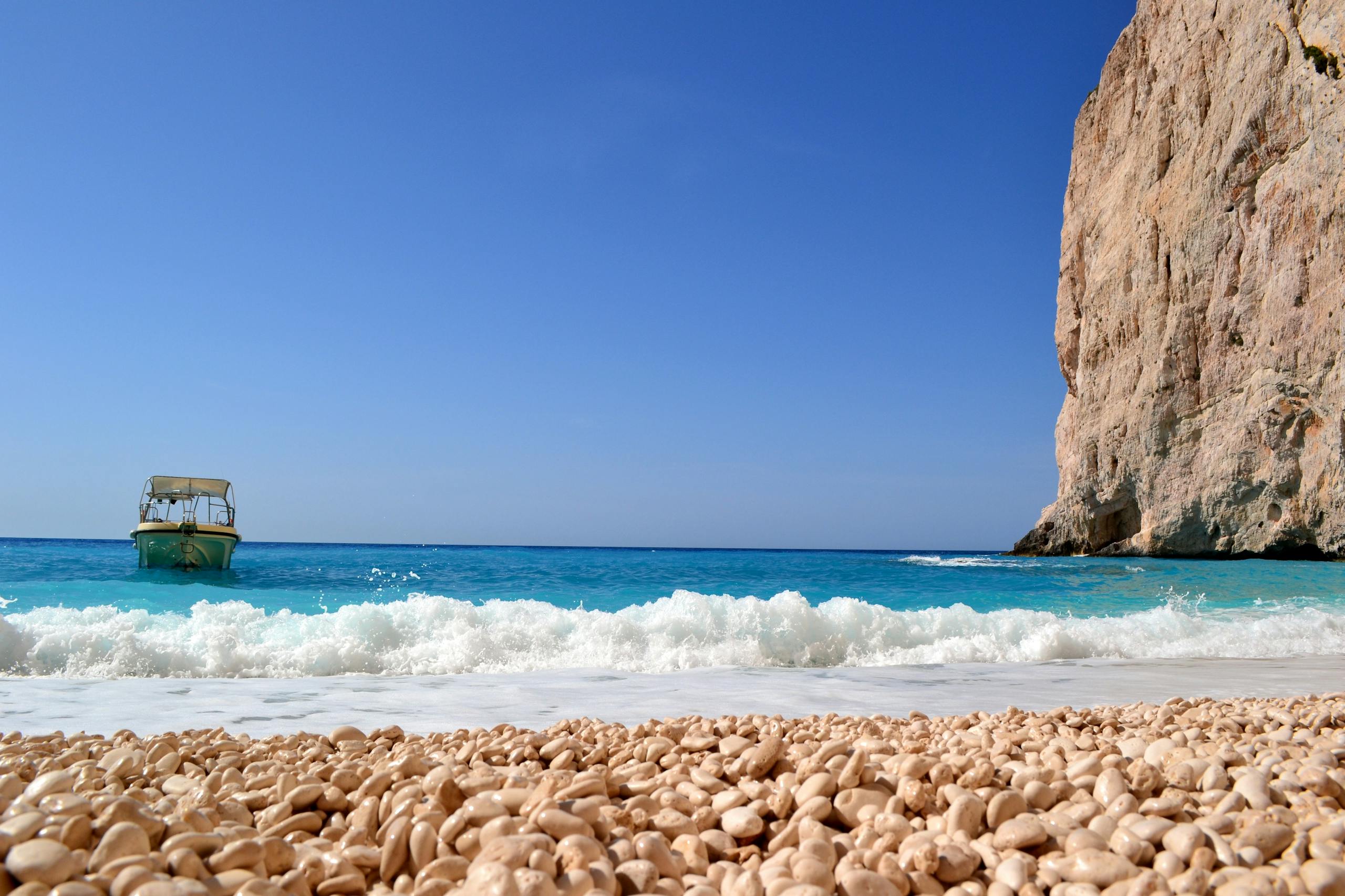 Voozon A peaceful seashore scene with a boat near a cliff and turquoise waters under a clear sky.