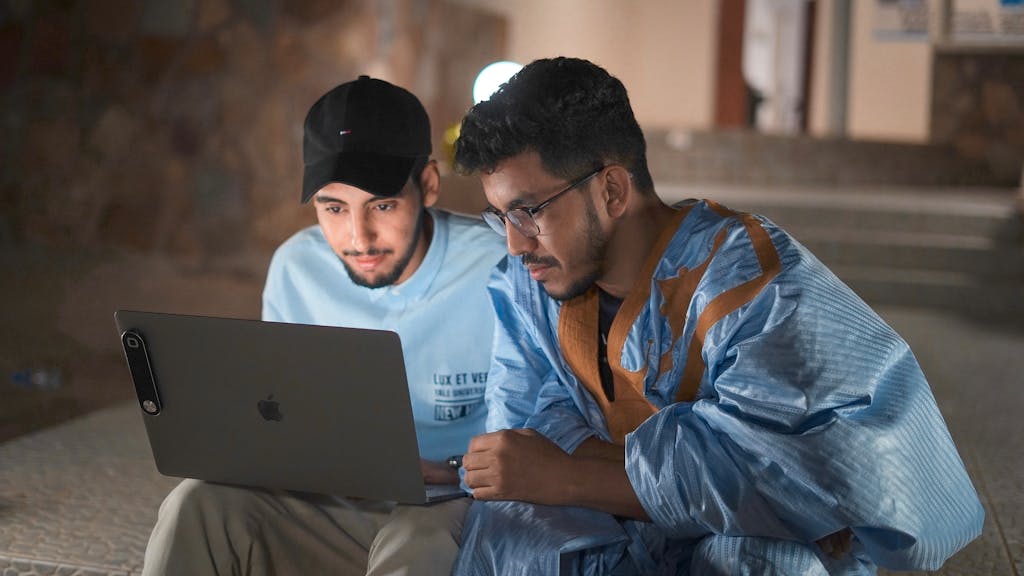 veb vatsap com Two men engaged in work on a laptop outdoors in Nouakchott at night.